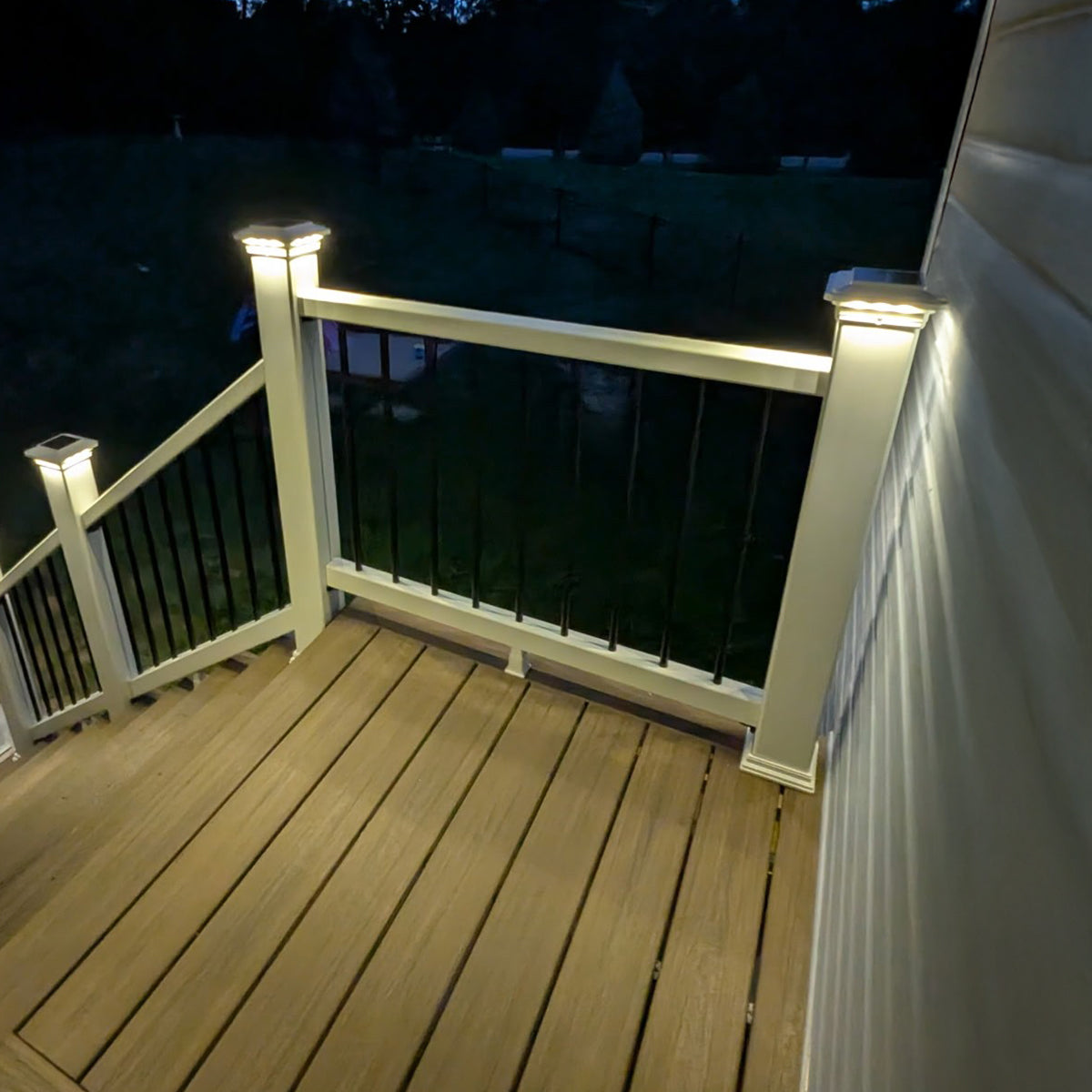Wooden deck with white railings and solar lights at night