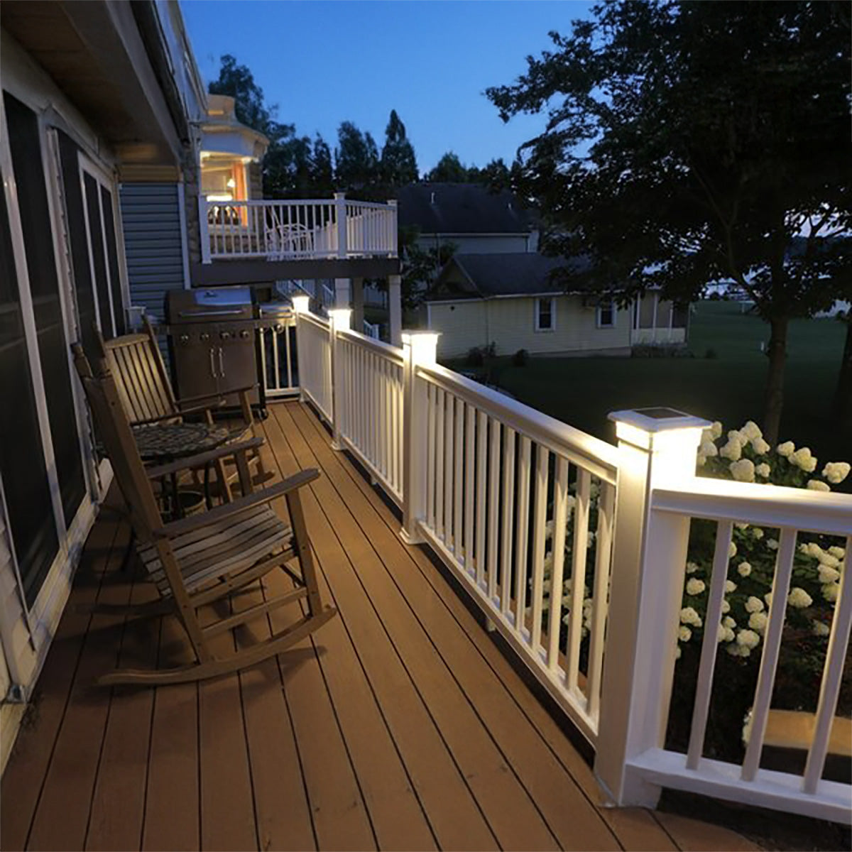 Backyard deck with rocking chairs, outdoor furniture, and lighting at dusk.