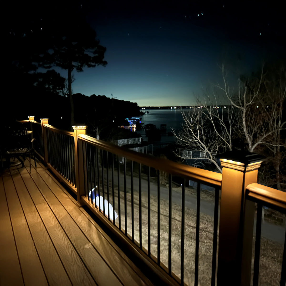 Wooden deck with railing overlooking a lake at night