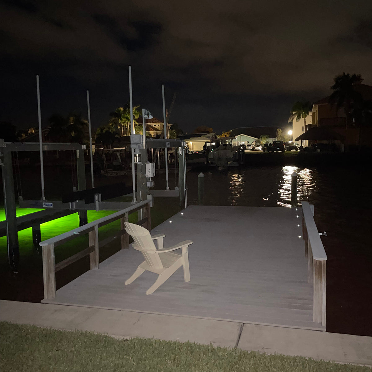 Dock with a chair at night, illuminated by green lights.