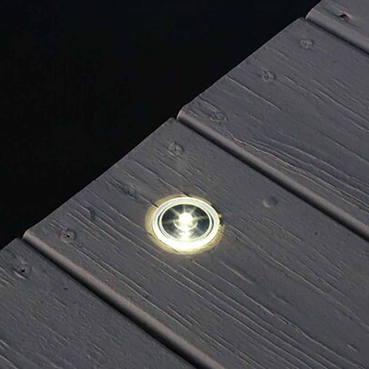 Close-up of a recessed light fixture on a dark gray wooden surface.