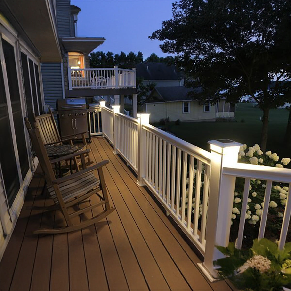 Evening view of a deck with rocking chairs, outdoor furniture, and decorative lights.
