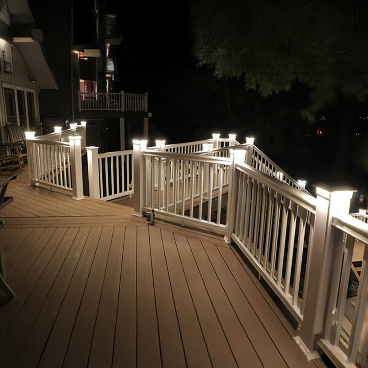 Wooden deck with white railings and outdoor lighting at night.