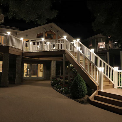 House exterior with a staircase and deck illuminated by lights at night.