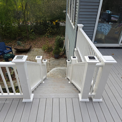 Gray deck with white railings leading to a house, surrounded by greenery.
