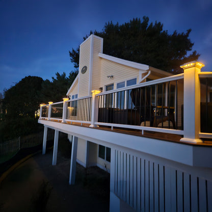 House with a large deck at night, surrounded by trees.