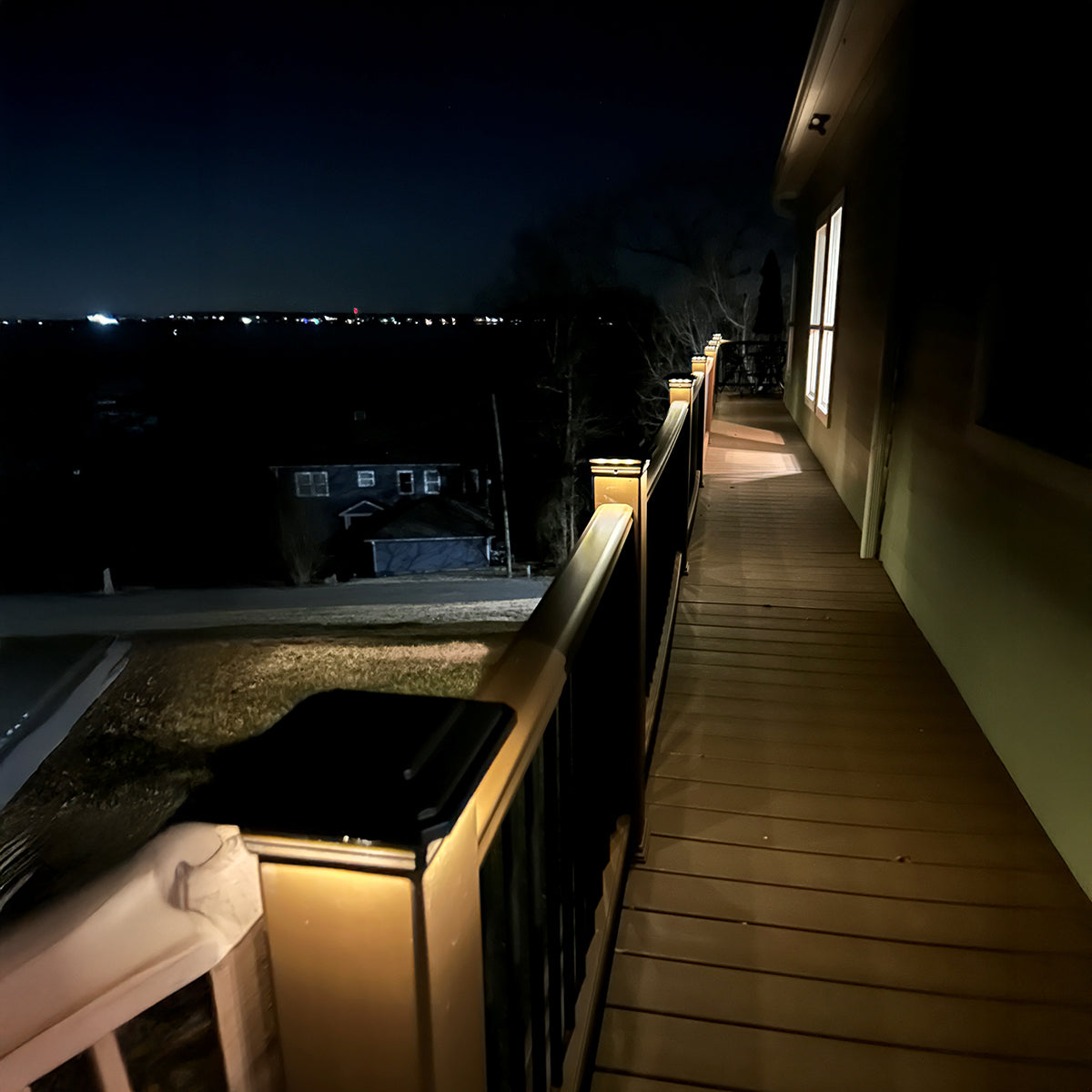 Balcony with wooden flooring and railing, illuminated by lights at night.