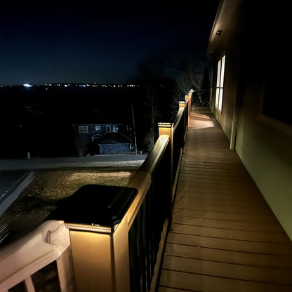 Balcony with wooden flooring and railing, illuminated by lights at night.